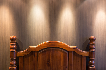 Wooden headboard in a dark bedroom lit by down lights on the ceilingの写真素材