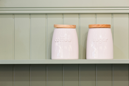 White ceramic coffee and sugar jars with wooden lid on a wooden green shelf wall.の写真素材