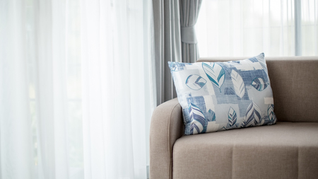 Beige color sofa with large pillow in a living room with large windows and white light curtain.の写真素材