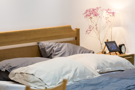 Comfy bed with wooden heardboard with white side bed lamp in a white bedroom.の写真素材