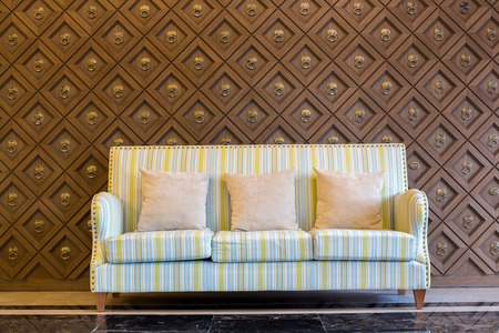 Stripes cloth sofa with three gray pillow in a luxury living room with wooden pattern wall and black granite floor.の写真素材