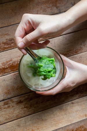 Woman holding full spoon of green chendol on a wooden table.の写真素材