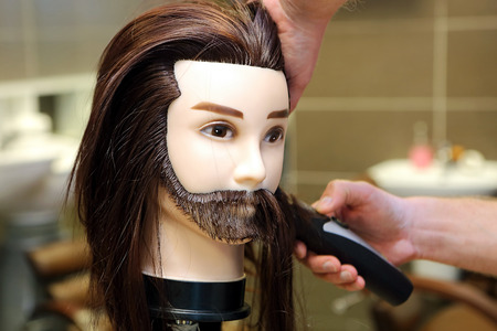 Barber student trimming brown hair using puppet and electric trimmerの写真素材