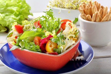 Fresh healthy salad in a bowl with grissini and sprouts on white wooden backgroundの写真素材