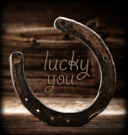 Old rusty horseshoe on wooden background with lucky you inscriptionの写真素材