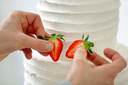 Confectioner decorates white wedding cake by fruitsの写真素材