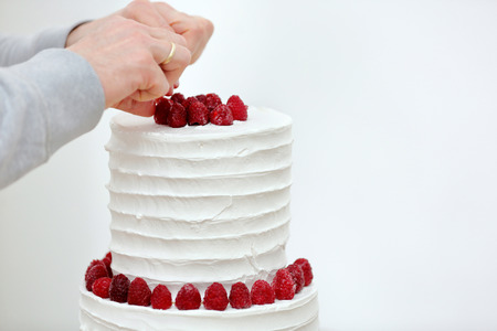 Confectioner decorates white wedding cake by fruitsの写真素材