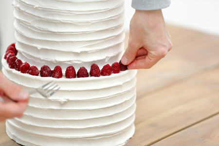 Confectioner decorates white wedding cake by fruitsの写真素材