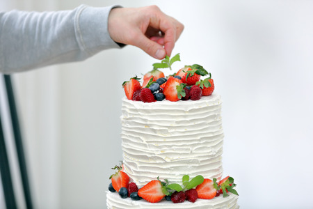 Confectioner decorates white wedding cake by fruitsの写真素材