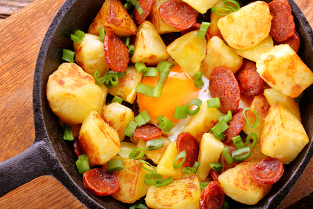 Baked potatoes with sausage chorizo and fried egg on frying panの写真素材