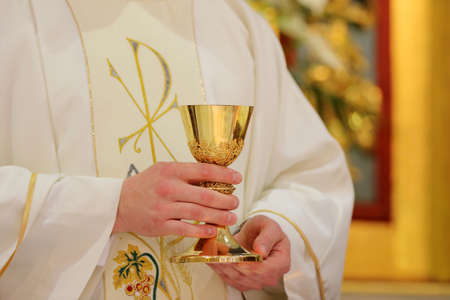 Chalice in the hands of the priest on the altar during the celebration of the mass and empty space for text