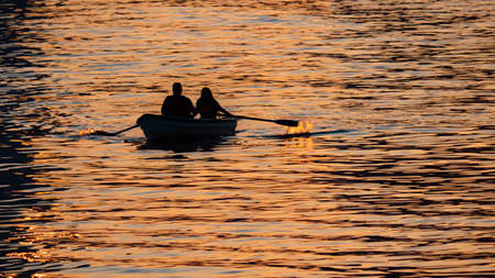 Relaxing at sunseta couple of people are sailing on a boat on the river, rowing oars