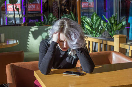 upset girl sits at the table. bad message on mobile phoneの写真素材