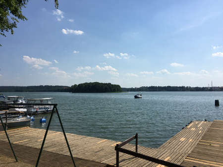 A view of the lake in MrÄgowo surrounded by forests and a blue skyの写真素材