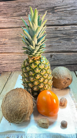 Pineapple on a jute napkin and oak boards, surrounded by coconuts, mangoes and walnuts and hazelnutsの写真素材