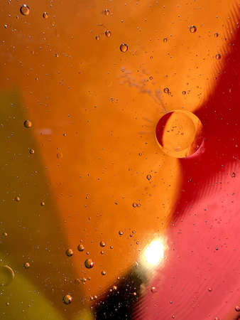 Floating oil drops shimmering in different colors and shapes next to air bubbles on a colored...