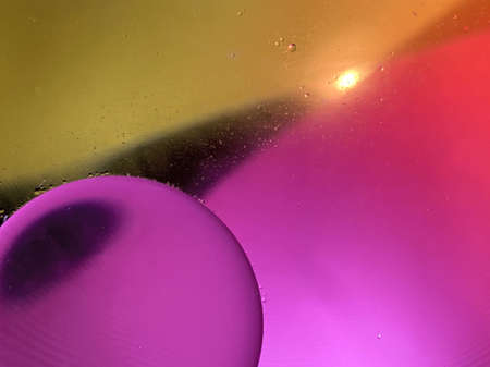 Floating oil drops shimmering in different colors and shapes next to air bubbles on a colored...