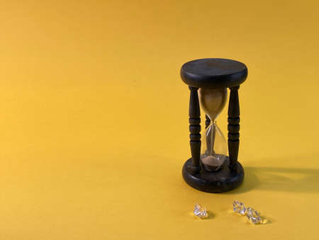 On a yellow background there is an hourglass measuring time scattered crystalsの写真素材