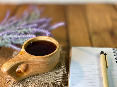 a table made of oak boards you can see jars on them there is a bouquet of lavender a wooden cup with coffee and a notebook and a pen a wall made of pine boards painted whiteの写真素材