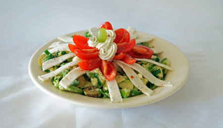 Healthy vegetarian salad with lots of vegetables, avocado, sliced spicy goat cheese, tomatoes, sauce (remoulade) and a grape on top.の写真素材