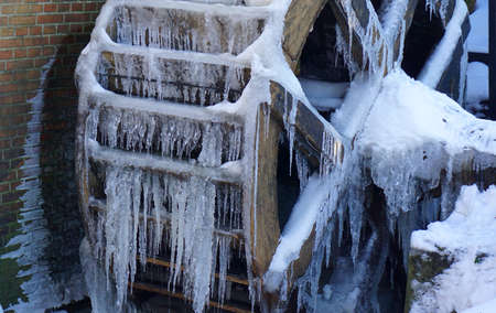 Wheel of a watermill. The water is partly frozen. Lots of icicles. Wintertime. It's cold