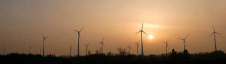 Panorama view on a wind farm at sunset. Silhouettes of wind turbines at sunset. A wind energy farm...