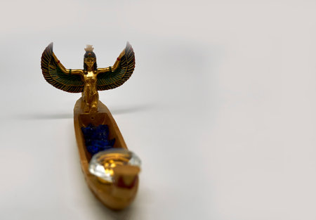 Embellished Egyptian souvenir. Golden boat with a winged goddess Isis. Isis has lost her headgear. On the boat are blue glass stones and a glass Crystal in diamond shape.の写真素材