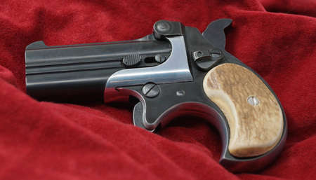 A double barrel derringer style pistol on a red velvet background. This kind of weapon was used by...