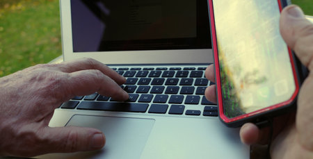 Hands of a man using a laptop and smartphone. He is sitting outside. Home office. Mobile working