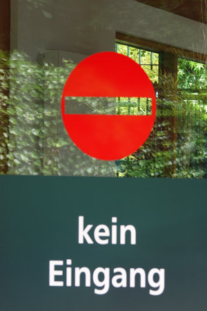 Glass door with the words 'kein Entrance' (German: no Entrance). A garden is reflected in the glassの写真素材