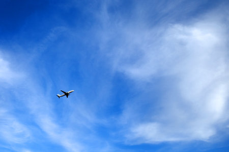 Airplane flying in a clear blue sky with wispy white clouds. The aircraft is positioned in the left...