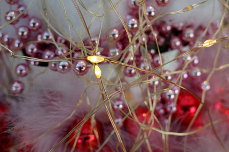Yellow LED lights with thin golden wire form a decorative display. Surrounding the lights are small, glossy pink pearl garlands with blurred red baubles. A festive Christmas decoration.の写真素材