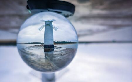 White Windmill at end of coast full of puddles near Baltic sea in Swinoujscie in reflection of...