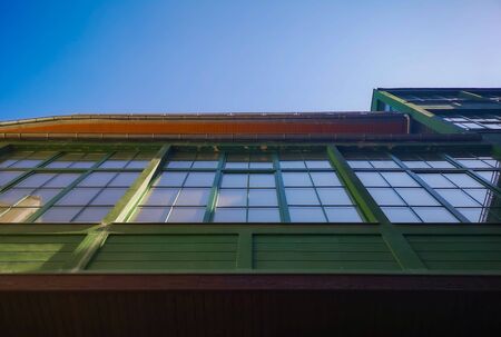 Upward look to wooden green walls of old tenement house with sky reflections in windowsの写真素材