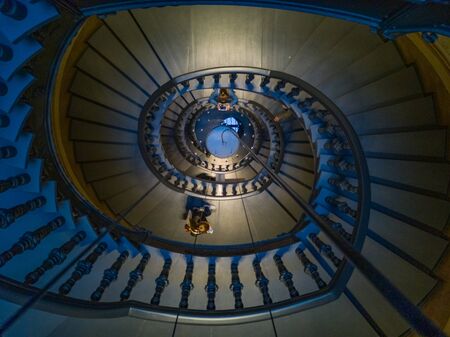 Dark spiral staircase with people walking around 