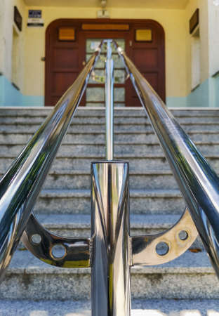 Metal chrome railing at stairs to the building with wooden doorsの写真素材