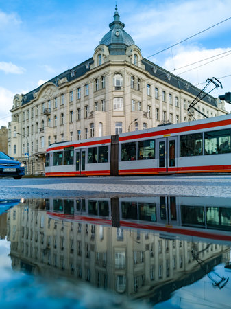 Lodz, Poland - February 21 2020 Red and gray driving tram in front of old tenement house reflected...