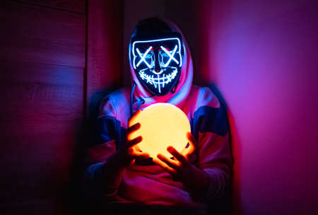 Man in glowing mask sitting in the corner with moon-shaped lampの写真素材