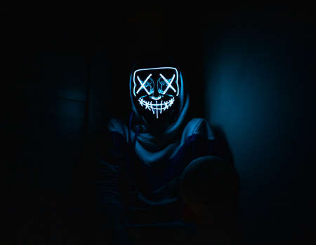 Man in glowing mask sitting in the cornerの写真素材