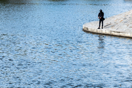 Man sitting on small concrete coast near river and fishingの写真素材