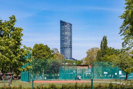 Wroclaw, Poland - May 8 2020: Top of Sky Tower skyscraper behind bushes trees and sport courtsのeditorial素材