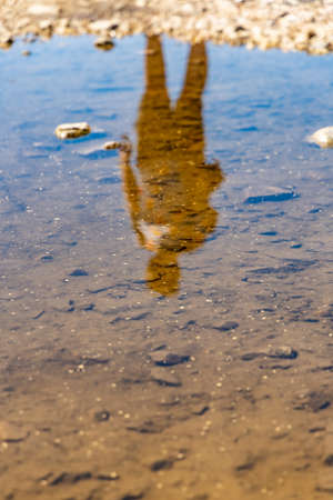 Silhouette of man reflecting in small puddle at sunny dayの写真素材