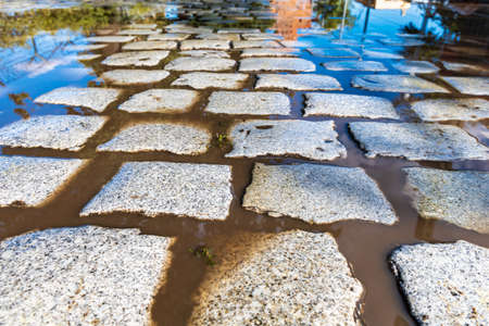 Long path full of gray stones like brick and water with reflections in puddlesの写真素材