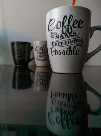 Black and white coffee cups standing and reflecting on black induction hobの写真素材