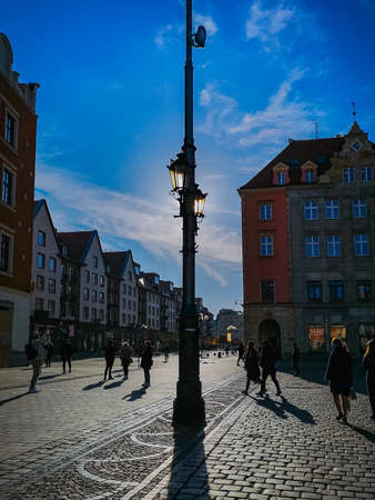 Wroclaw, Poland - November 21 2020: Sun shining behind old lantern at market square full of people