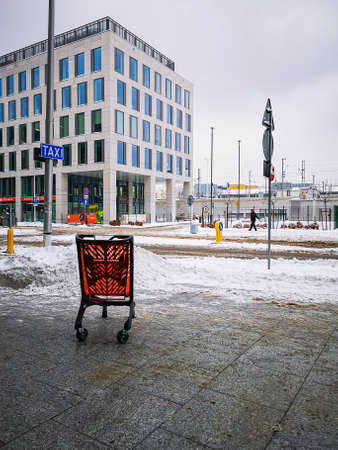 Wroclaw, Poland - February 2021: Red shopping cart standing on sidewalk next to shopping mall at winter cloudy dayのeditorial素材