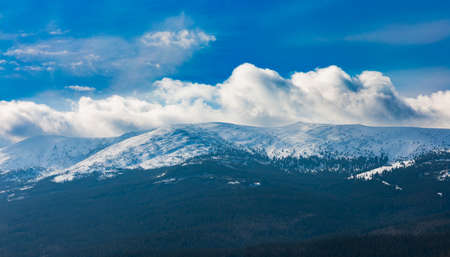 Foggy cloudy landscape seen from long distance of mountain ranges full of snow and giant clouds over itの写真素材