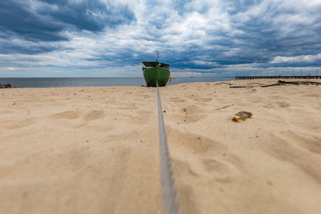 Long steel wire connected to small wooden ferry standing on a beach at cloudy dayの写真素材