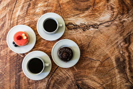 Colorful small fruity cupcakes on small white plates and cups of black coffee on wooden structure backgroundの写真素材