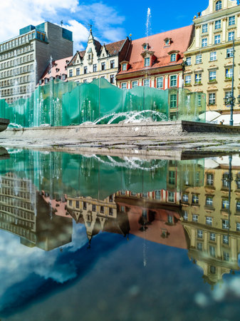 Wroclaw, Poland - May 2022: Beautiful fountain at center of market square reflected in small puddle at sunny cloudy dayのeditorial素材